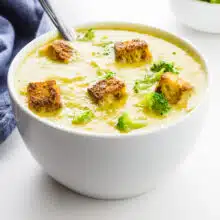 A bowl of vegan broccoli soup has croutons on top.