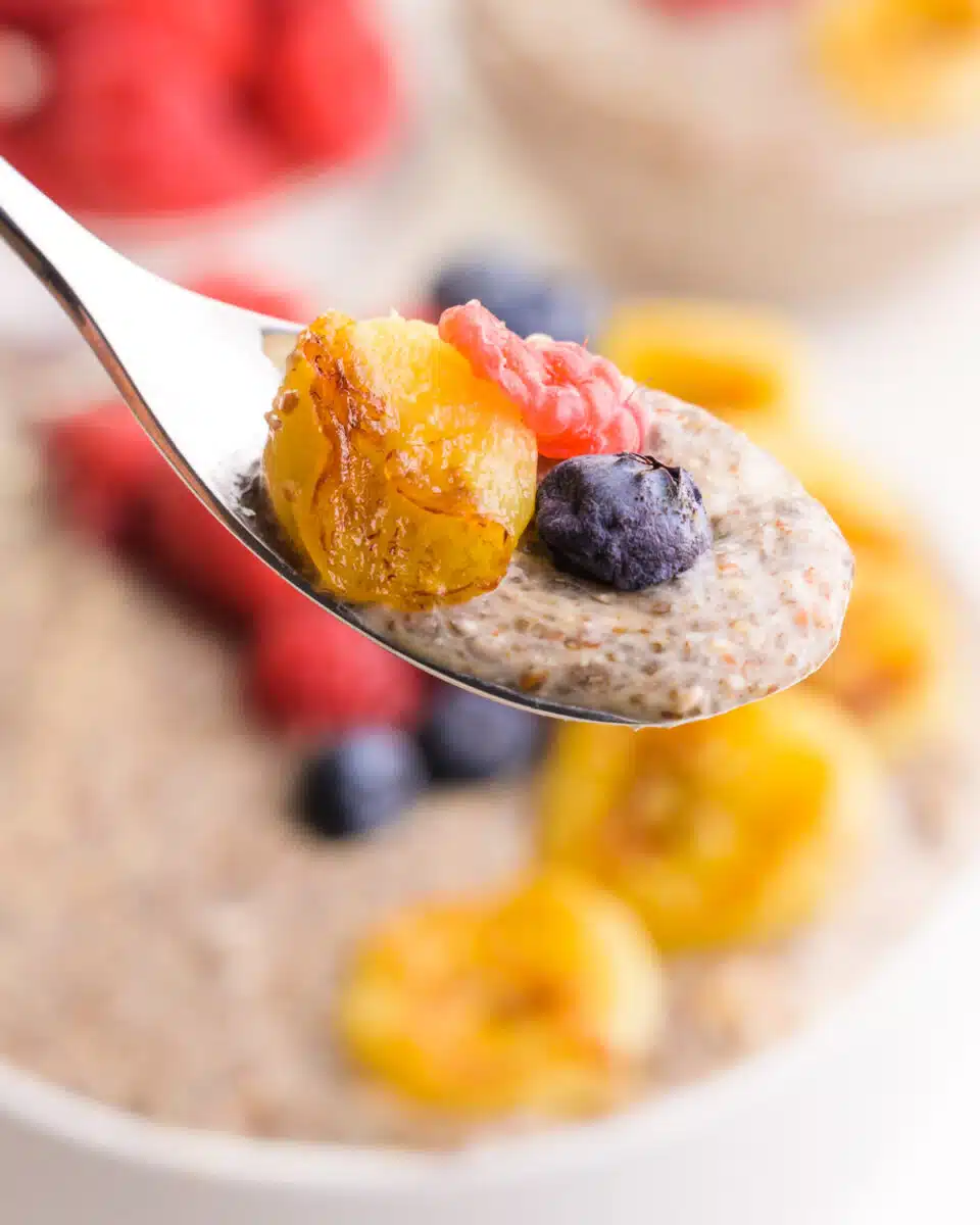 A spoonful of hot chia pudding has a bit of berries and bananas in it. It hovers over the rest of the bowl with fresh berries in the background.