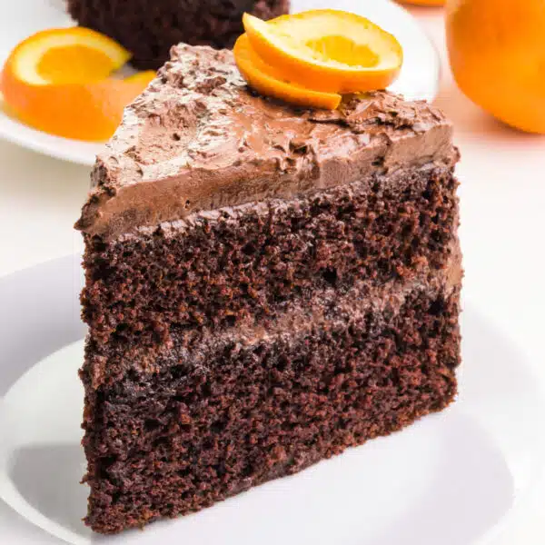 A slice of eggless orange chocolate cake sits on a plate. There is a orange slice on top of the cake.