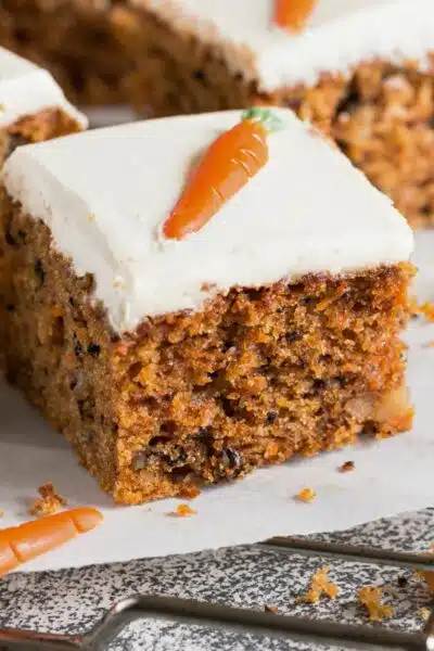 A slice of cake has white frosting and orange frosting in the shape of a carrot.