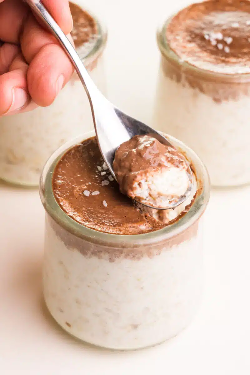 A spoon dishes out a bite of dairy-free bounty overnight oats. There are two jars visible in the background.
