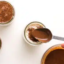 Chocolate sauce is being poured with a spoon over overnight oats.