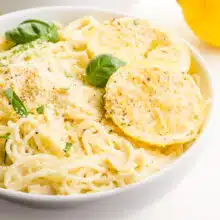 A closeup of lemon slices on a bowl of pasta with fresh basil on top.