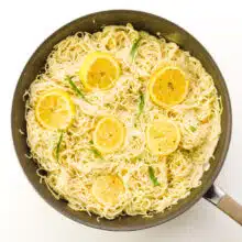 Looking down on lemon slices and basil on top of pasta in a pan.