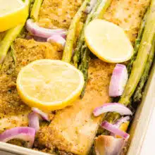 A pan holds lemon pepper tofu, red onions, asparagus, and lemon wedges.