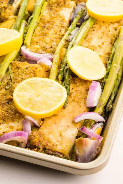 A pan holds lemon pepper tofu, red onions, asparagus, and lemon wedges.