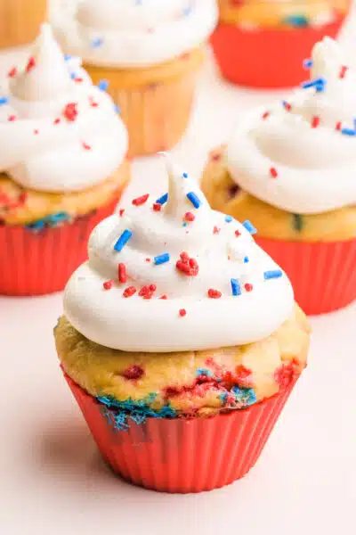 Patriotic cupcakes are in red silicone cupcake liners. They're topped with white frosting and red, white, and blue sprinkles.