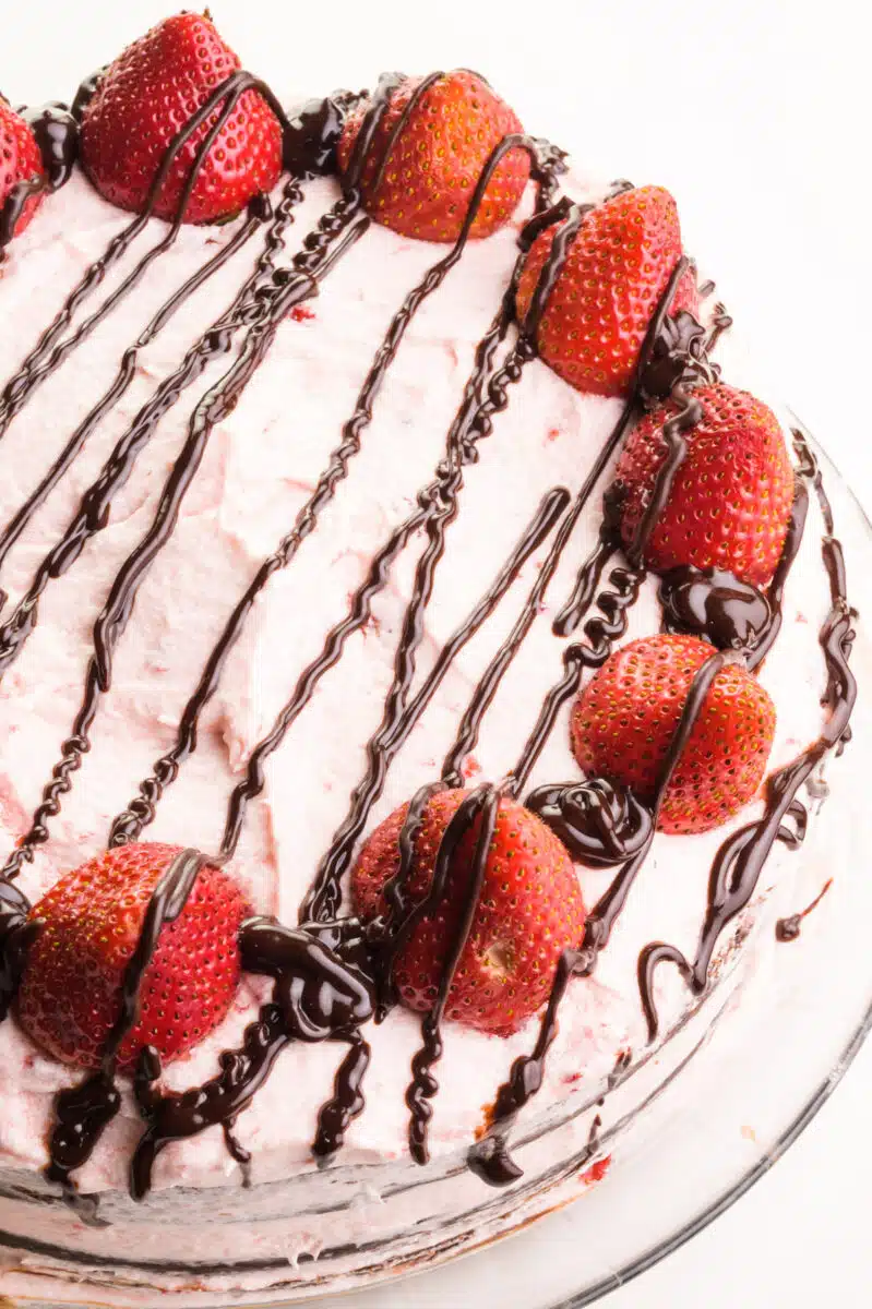 Looking down on a cake with pink frosting, fresh strawberries, and chocolate drizzles.