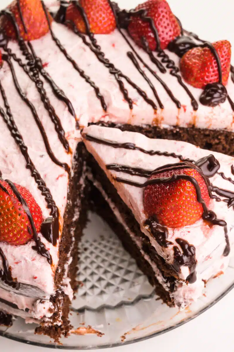 Looking down on a chocolate strawberry cake with a slice cut out. There are fresh strawberries and chocolate drizzles on top of the cake.
