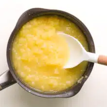 A spoon stirs a pineapple mixture in a saucepan.