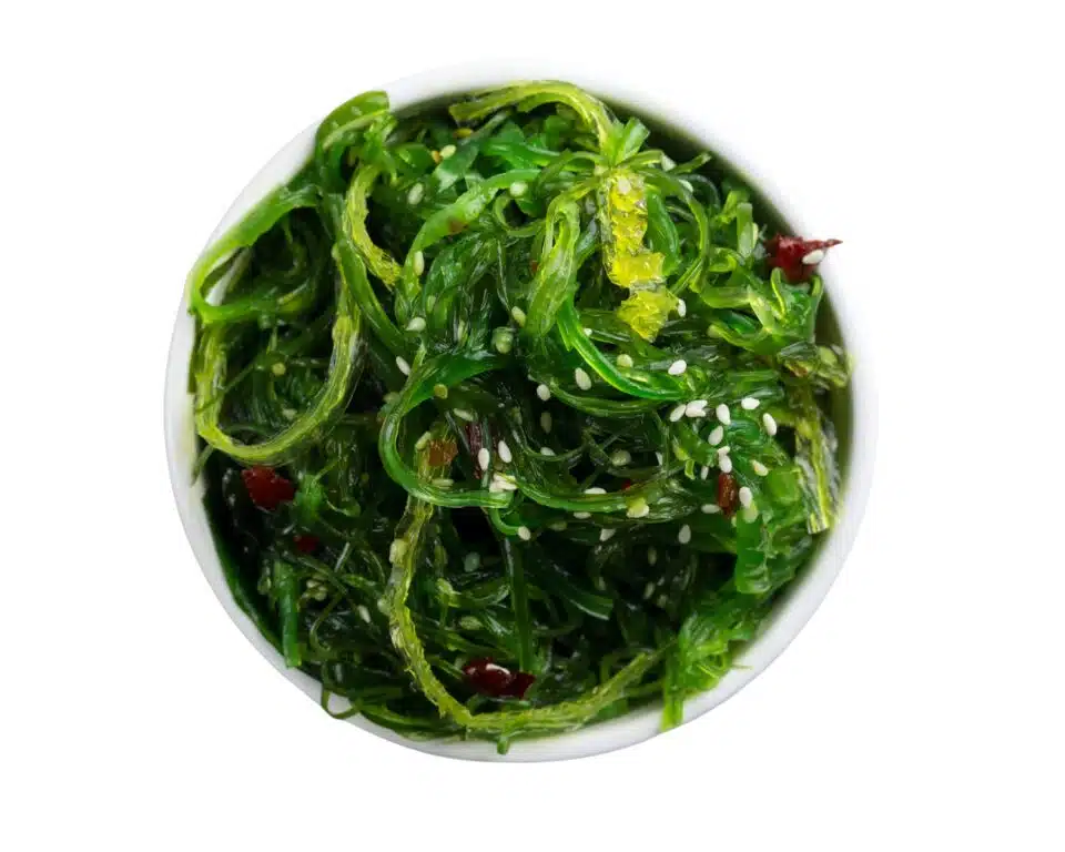 A bowl of bright green wakame seaweed is in a white bowl on a white counter.
