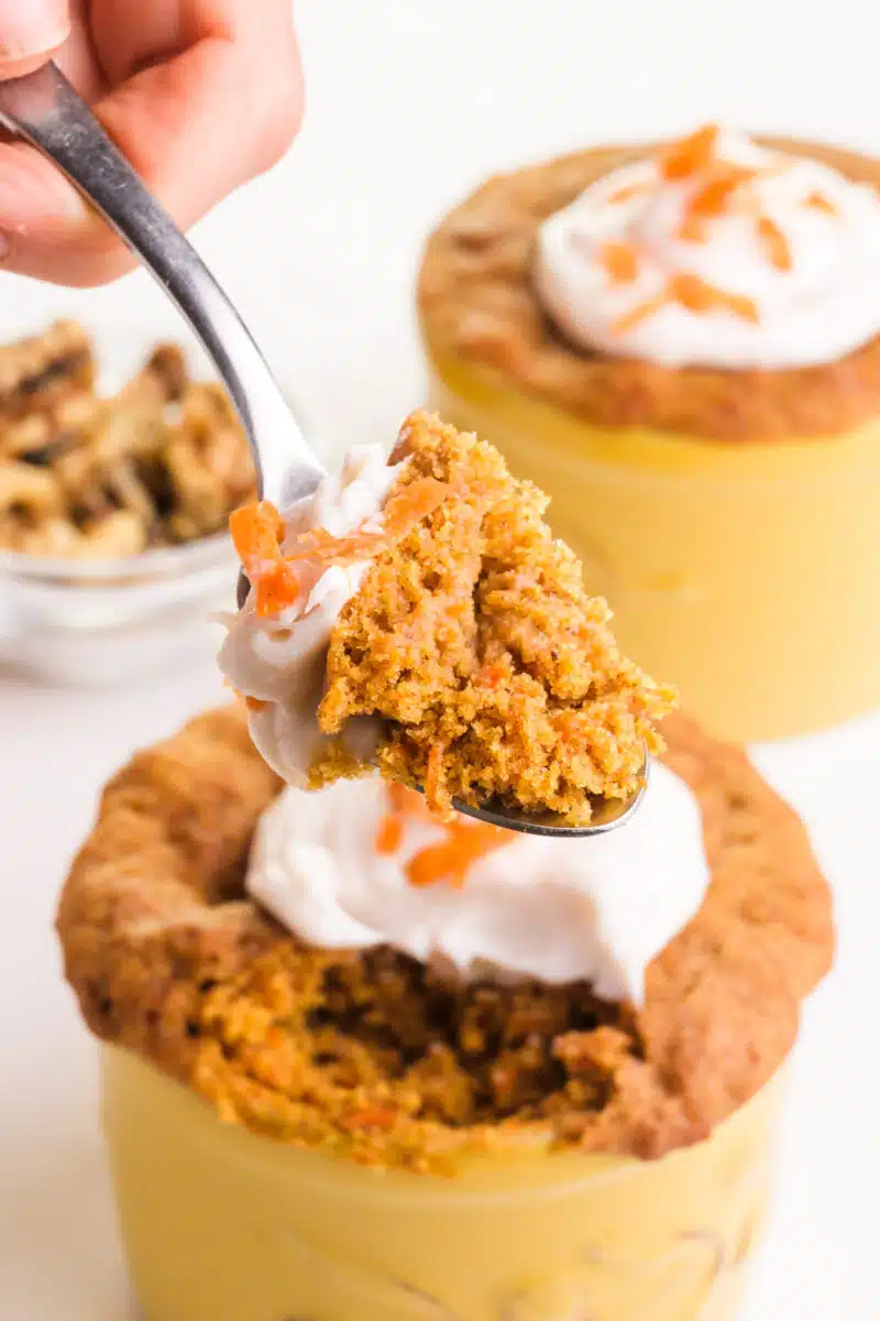 A spoonful of carrot cake mug cake hovers in front of more of the dishes in the background, including a bowl of walnuts.