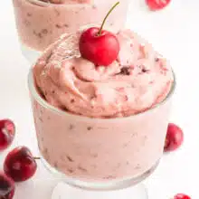 A bowl of cherry banana ice cream has a fresh cherry on top and more cherries around it.