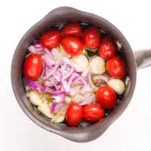 Tomatoes, garlic, and red onions are cooking in a saucepan.