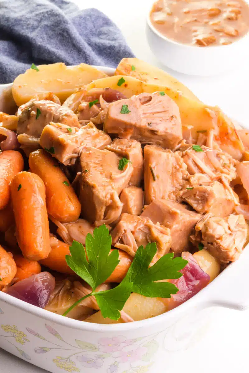 A baking dish holds jackfruit pot roast with cooked carrots and potatoes. There is a kitchen towel and gravy in the background.
