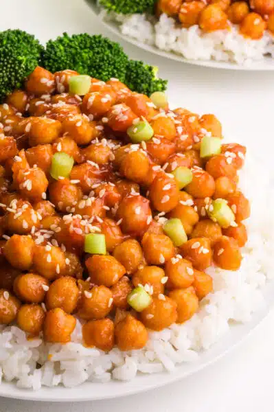 A plate of rice topped with sticky sesame chickpeas has broccoli on it, too. There's another plate visible in the background.