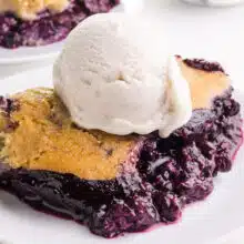 A slice of vegan blueberry cobbler on a plate with ice cream on top.