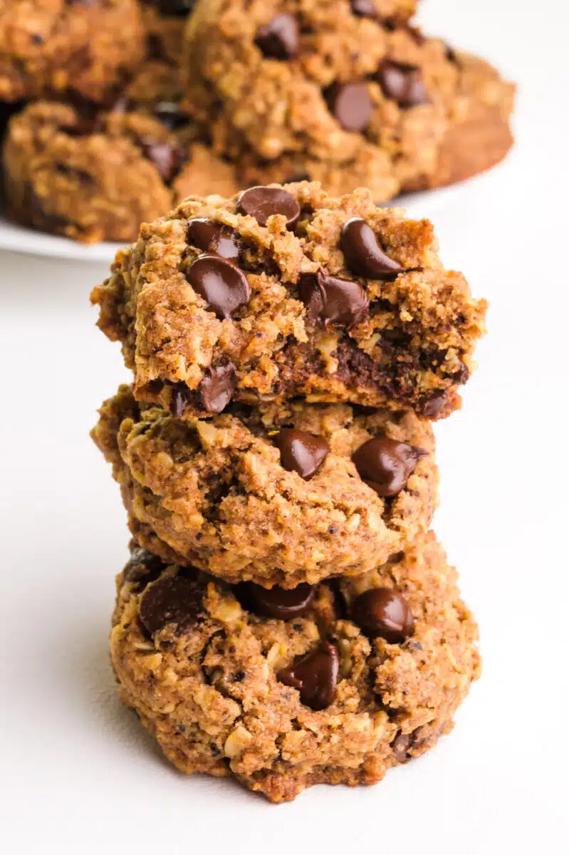 A stack of vegan coffee cookies shows the top one with a bite taken out. There is a plate with more cookies in the background.