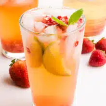A glass of strawberry green tea sits in front of two glasses and fresh strawberries in the background.