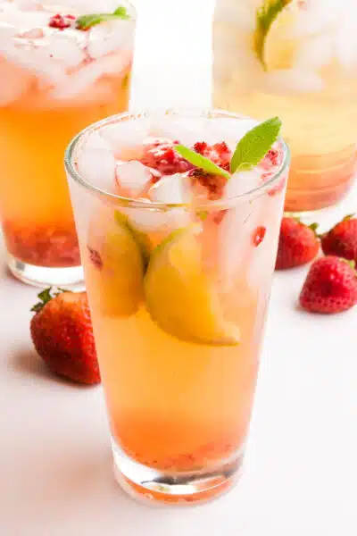 A glass of strawberry green tea sits in front of more glasses of the beverage. There are fresh strawberries in the background.